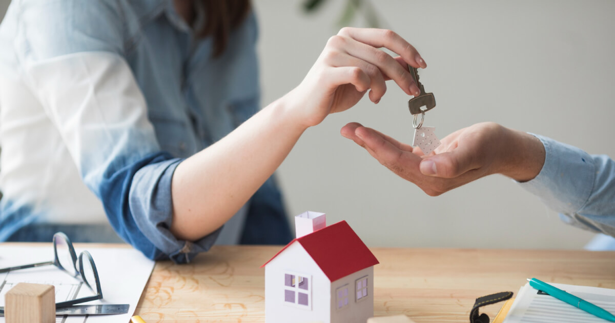 Close-up of hands exchanging keys over a model home, representing proven strategies to sell your house fast in the real estate market.